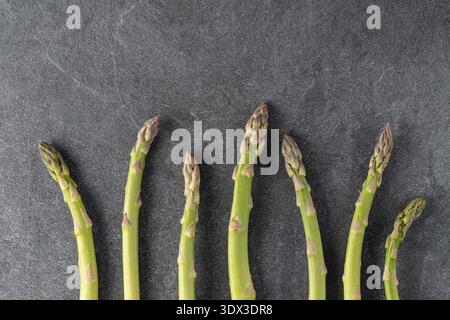 Asperges crues vertes sur table en pierre grise. Légume de printemps de saison pour une alimentation saine. Fond sombre avec espace de copie. Banque D'Images