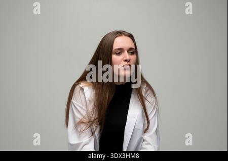 Jeune femme avec de longs cheveux regardant loin, exprimant le doute et l'incertitude sur un fond Uni Banque D'Images