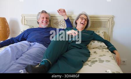 Couple senior riant ensemble dans le lit profitant du matin Banque D'Images