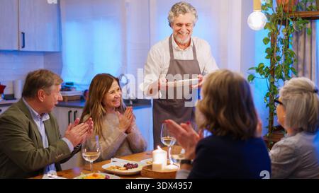 Homme senior souriant servant de la nourriture à des amis applaudissants Banque D'Images