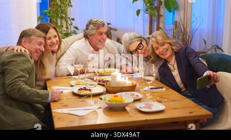 Amis prenant un selfie de groupe à un souper joyeux Banque D'Images