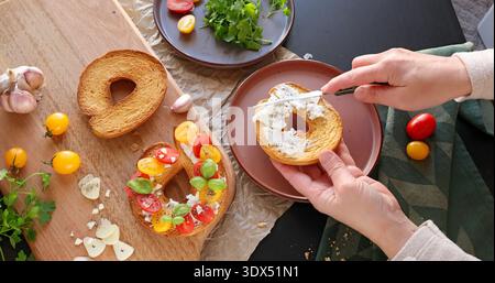 Une personne anonyme prépare une bruschetta ronde avec du fromage de chèvre crémeux et des tomates cerises dans la cuisine. Cuisine italienne, de haute qualité cultivée à la ferme Banque D'Images