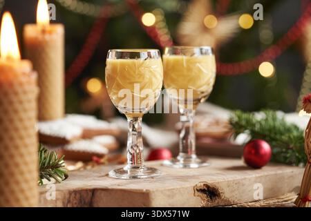 Eiercognac dans deux tasses en verre coupées avec des bougies et arbre de Noël et décoration sur une table Banque D'Images