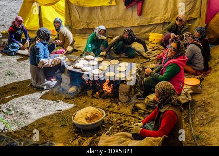Les femmes locales de Sagnam font cuire des pains plats traditionnels sur un feu ouvert sous une tente, assises ensemble dans un cercle social pendant la préparation des repas. Banque D'Images