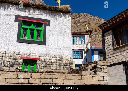 La façade d'une maison traditionnelle dans la boue présente des cadres de fenêtres vert vif et un toit de chaume, avec des pentes de montagne rocheuses visibles derrière. Banque D'Images
