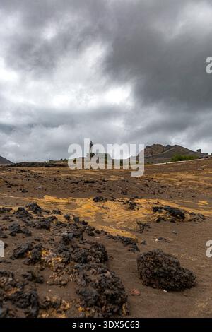 Faial, les îles Açores, Portugal paysage désolant avec une grande formation rocheuse et un phare au loin. Le ciel est nuageux et l'ensemble du ciel est rougeoyable Banque D'Images