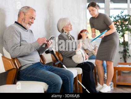 Les personnes âgées font la queue pour voir un travailleur social. Le secrétaire ou le travailleur social peut être entendu parler en arrière-plan Banque D'Images