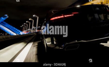 Voiture noire qui accélère sur une autoroute la nuit, montrant les feux arrière et les lampadaires flous en mouvement. Concept de transport moderne Banque D'Images