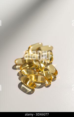Une collection de suppléments vitaminiques encapsulés dans des capsules de gel souples, présentés sur une surface blanche. Les capsules transparentes réfléchissent la lumière, accentuzi Banque D'Images
