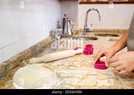 Mains façonnant la pâte à biscuits maison à l'aide de couteaux colorés sur un comptoir de cuisine, illustrant la joie et la créativité de la cuisson à la maison avec Handmad Banque D'Images