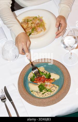 Un cadre de restaurant gastronomique avec des plats élégamment plaqués sur une nappe blanche. Les fruits de mer et les légumes parfaitement présentés invitent à une cuisine raffinée Banque D'Images