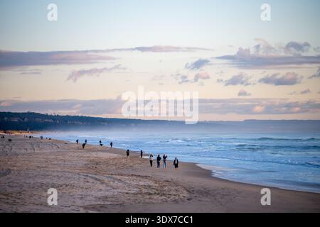 Large plage de sable avec des gens marchant le long du rivage de l'Atlantique pendant la lumière du jour de la saison froide à Costa da Caparica. Banque D'Images