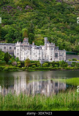 L'abbaye de Kylemore se reflète dans Pollacappul Lough, avec des roseaux et des nénuphars au premier plan et à flanc de colline derrière, Connemara, Co. Galway, Irlande. Banque D'Images