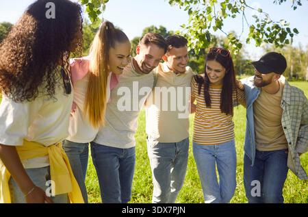 Heureux amis debout étroitement embrassant dans le parc vert d'été ensoleillé, groupe amical diversifié souriant Banque D'Images