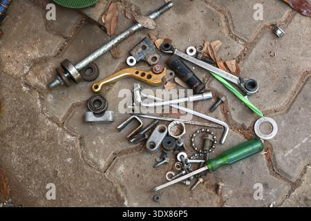 Pile désordonnée de pièces de rechange de moto et d'outils dispersés sur le plancher d'atelier en béton pendant le projet d'entretien ou de réparation. collection de divers métaux Banque D'Images