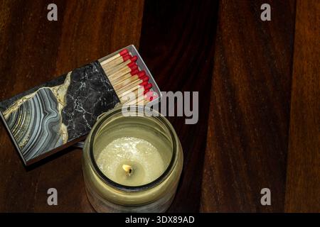 bougie allumée dans un pot en verre avec des allumettes sur une surface en bois Banque D'Images