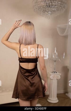 Jeune femme en robe brune brillante posant près d'une colonne blanche Banque D'Images