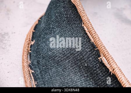 Gros plan d'un tapis de jute tressé bordant un tissu tissé gris foncé, mettant l'accent sur la texture organique et l'artisanat Banque D'Images