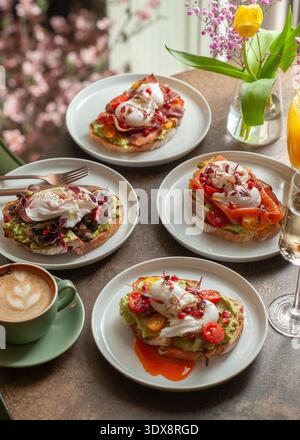 Une table de brunch magnifiquement stylisée avec quatre toasts à l'avocat différents surmontés d'œufs pochés, bacon, champignons, saumon et tomates, accentué avec Banque D'Images