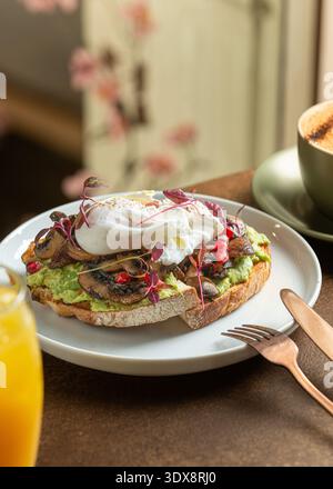 Une photo en hauteur d'un brunch gastronomique composé d'une purée crémeuse d'avocat, de champignons terreux sautés et d'un œuf poché doux sur du pain au levain grillé. Banque D'Images