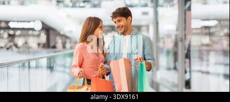 Jeune couple porte des sacs à provisions tout en marchant dans le centre commercial pendant l'après-midi Banque D'Images