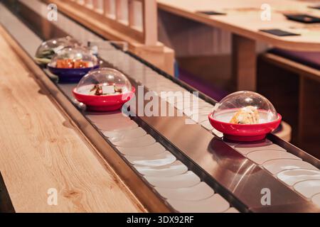 Plats de sushi se déplaçant le long d'un tapis roulant à l'intérieur d'un restaurant japonais moderne Banque D'Images