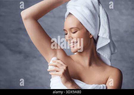 Femme appliquant le déodorant dans la salle de bain après la douche portant une serviette sur sa tête et son corps Banque D'Images