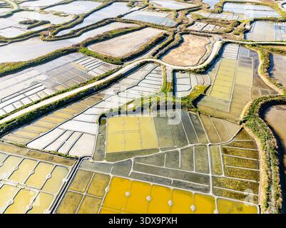 Vue aérienne de salines géométriques chatoyantes sous le soleil, créant une mosaïque de teintes dorées et argentées dans le paysage, Guérande, Bretagne, France. Banque D'Images