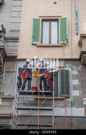 Milan Italie 27 février 2026 : deux ouvriers portant des casques et des équipements de sécurité travaillent sur des échafaudages métalliques lors de travaux de maintenance et de rénovation Banque D'Images