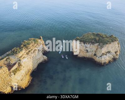 Vue aérienne des falaises escarpées embrassant la mer tranquille, où les paddleboarders dansent à la surface de l'eau, créant un paysage marin fascinant, Lagos, Fa Banque D'Images