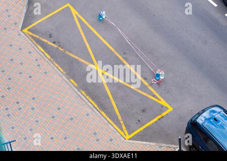 Panneau rectangulaire jaune interdisant le stationnement sur asphalte. Les ouvriers appliquent des marquages routiers avec de la peinture. Pas de vue de dessus de la ligne de zone de stationnement. Banque D'Images