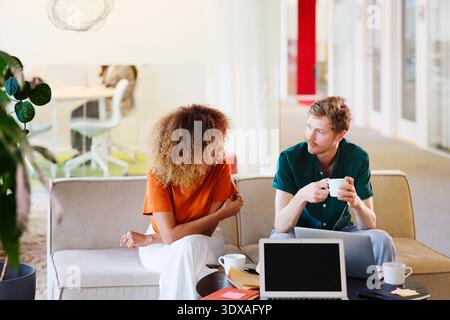 Collègues hommes et femmes d'affaires parlant entre eux tout en étant assis sur le canapé dans le bureau Banque D'Images