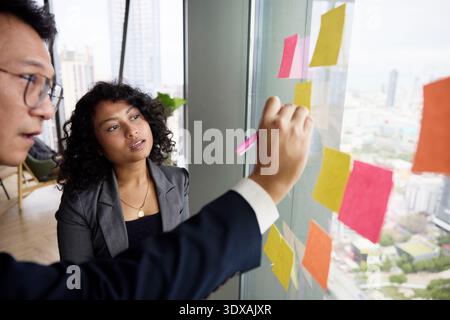 Collègue à côté du directeur écrivant sur une note adhésive au bureau Banque D'Images