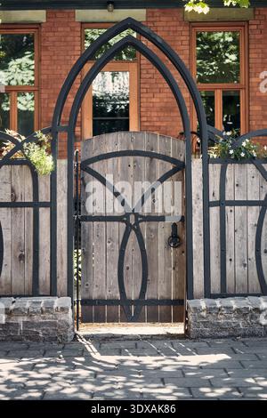 Portail en bois orné avec arc gothique en fer forgé et détails décoratifs, formant une entrée à une maison en briques Banque D'Images