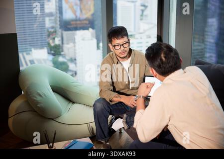 Vue en angle élevé des stratégies de planification des entrepreneurs masculins tout en étant assis sur le canapé au bureau Banque D'Images