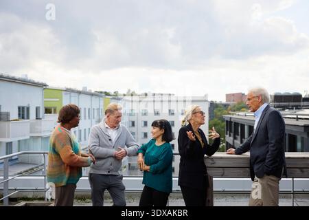 Groupe de professionnels des affaires masculins et féminins discutant les uns avec les autres tout en se tenant debout sur la terrasse de l'immeuble de bureaux pendant l'heure de pause Banque D'Images