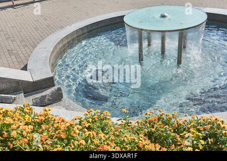 Gros plan vue en angle élevé d'une fontaine publique entourée de fleurs de pensées orangées dans le centre-ville, Rybnik, Silésie, Pologne, Europe. Banque D'Images