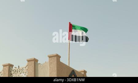 Drapeau national des Émirats arabes Unis, avec les couleurs rouge, vert, blanc et noir, ondulant au vent contre un ciel bleu clair. Banque D'Images