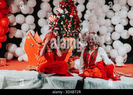 Deux filles en costumes rouges se produisent sur une scène festive avec un décor de sapin de Noël Banque D'Images