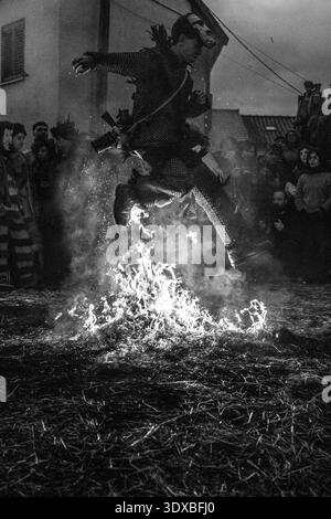 Le 17 février 2026, Un personnage masqué dans un masque de diable en bois sculpté à la main saute sur des braises pendant le carnaval médiéval d'Entrudo à Vila Boa de Ousilhao Banque D'Images