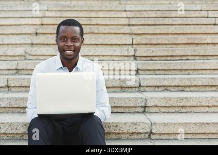 Homme travaille sur ordinateur portable tout en étant assis sur les marches pendant la journée Banque D'Images