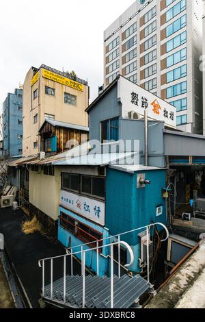 Marché extérieur de Tsukiji, Tokyo, Japon - vieilles boutiques délabrées avec parement en métal ondulé, fils électriques complexes et gratte-ciel modernes à l'arrière Banque D'Images