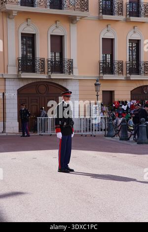 Garde de cérémonie debout à l'attention devant le Palais Prince à Monaco avec façade rose, portes voûtées et touristes en arrière-plan.Monte Carlo, Monaco Banque D'Images