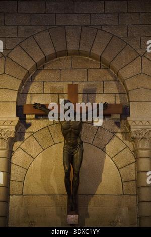Statue crucifix en bronze du Christ dans une niche en pierre voûtée illuminée la nuit dans la chapelle ou la cathédrale de Monaco.Monte Carlo, Monaco Banque D'Images