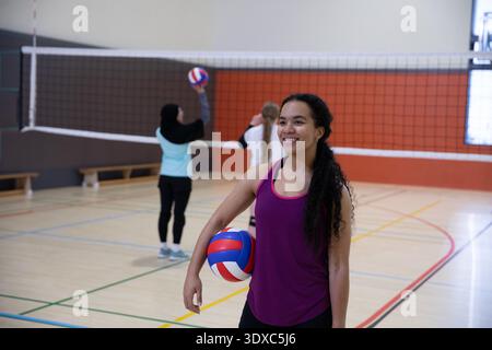 Diverses coéquipières féminines pratiquant le volley-ball sur un terrain de gymnastique avec filet, balle rouge, hijab, espace copie Banque D'Images