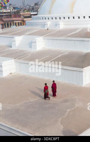 Deux moines bouddhistes en robe marron marchant sur la vaste base blanche du Boudhanath Stupa, Katmandou, Népal. Banque D'Images
