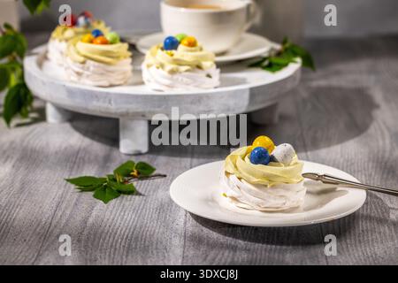 De doux mini nids de meringue pavlova créant de charmants plateaux de desserts, surmontés de tourbillons crémeux et d'œufs de pâques au chocolat vifs pour un printemps festif Banque D'Images