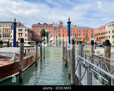 Des bateaux et des postes d'amarrage en bois bordent un canal à Venise tandis que les bâtiments historiques du front de mer réfléchissent sur l'eau. Banque D'Images
