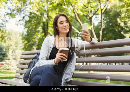 Jeune personne profitant du café et de la musique tout en étant assis sur un banc de parc Banque D'Images