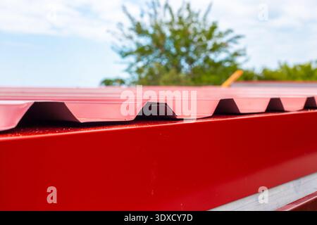 Gros plan du bord d'un toit en métal ondulé rouge contre un ciel mou. texture industrielle, motif métallique, détail de construction. Banque D'Images